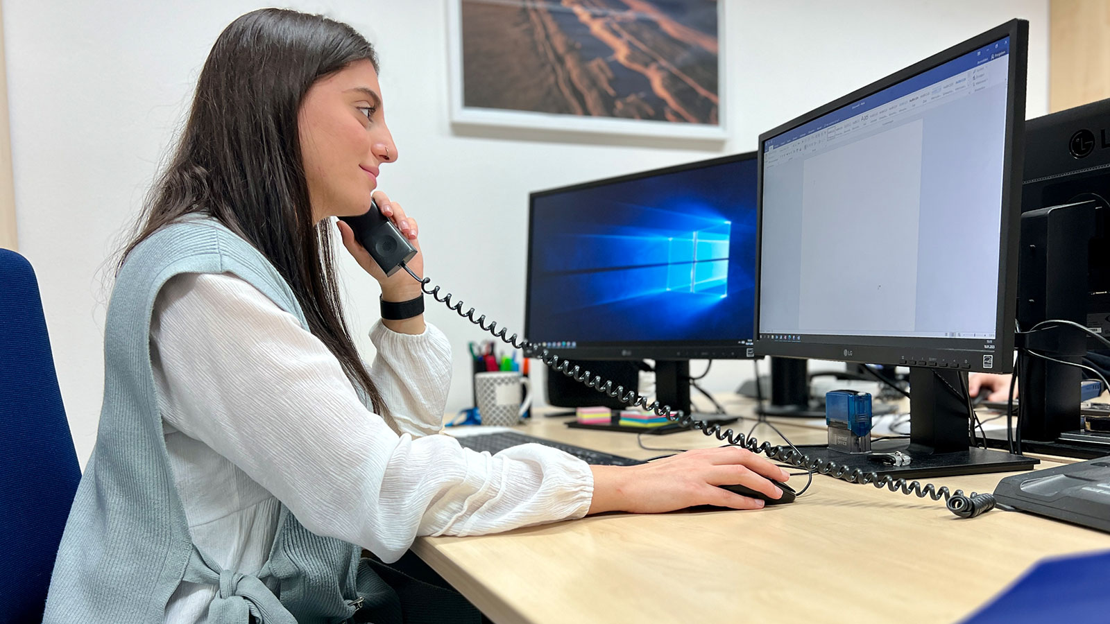 Frau sitzt am Schreibtisch vor dem Computer und telefoniert